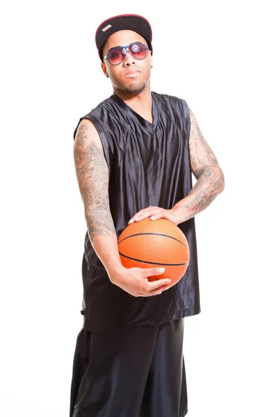 Studio portrait of basketball player wearing cap and sunglasses standing and holding ball isolated on white. Tattoos on his arms. — Stock Photo, Image