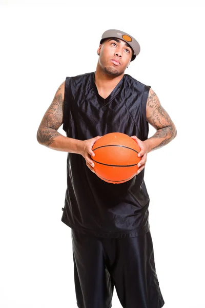 Студийный портрет баскетболиста в белой кепке, стоящего и держащего мяч изолирован на белом. Татуировки на руках . — стоковое фото