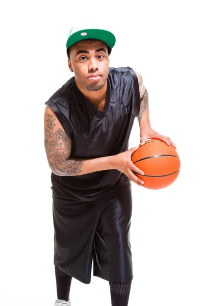 Retrato de estudio del jugador de baloncesto con gorra verde de pie y sosteniendo la pelota aislada en blanco. Tatuajes en sus brazos . —  Fotos de Stock