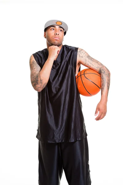 篮球运动员戴着白帽子站和持有球上白色隔离室画像。他手臂上的纹身. — 图库照片