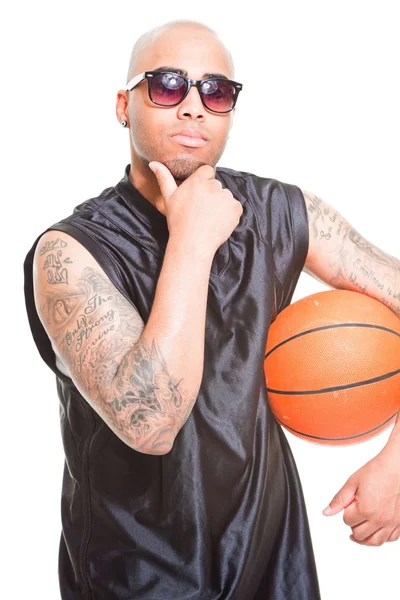 Retrato de estudio del jugador de baloncesto con gafas de sol negras de pie y sosteniendo la pelota aislada en blanco. Tatuajes en sus brazos . — Foto de Stock