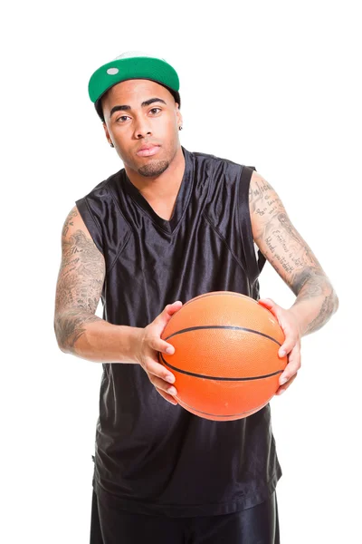 Studio portrait of basketball player wearing green cap standing and holding ball isolated on white. Tattoos on his arms. — Stock Photo, Image