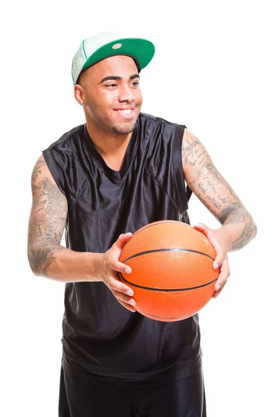 Studio portrét basketbalový hráč na sobě zelenou čepici stojí a drží míč izolovaných na bílém. tetování na ruce. — Stock fotografie