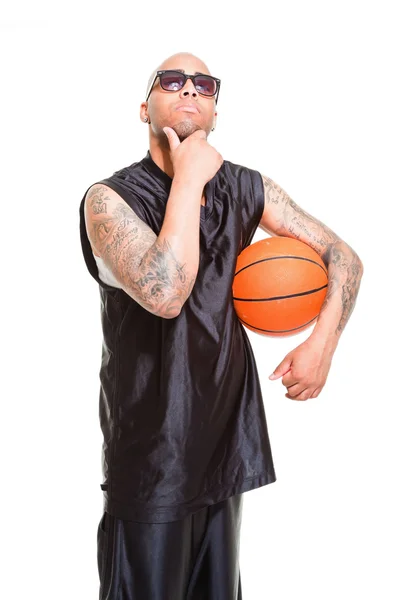 Studioporträt eines Basketballspielers mit schwarzer Sonnenbrille stehend und Ball isoliert auf weiß haltend. Tätowierungen auf seinen Armen. — Stockfoto
