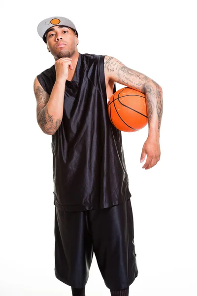 Estúdio retrato de jogador de basquete vestindo boné branco de pé e segurando bola isolada em branco. Tatuagens em seus braços . — Fotografia de Stock