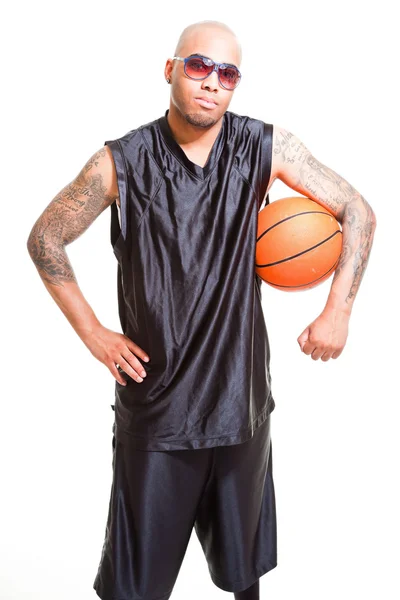 Studioporträt eines Basketballspielers mit schwarzer Sonnenbrille stehend und Ball isoliert auf weiß haltend. Tätowierungen auf seinen Armen. — Stockfoto