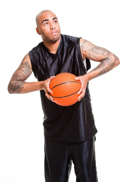 Portret van een jonge basketbalspeler die permanent met een bal tegen witte achtergrond. studio opname. tatoeages op zijn armen. — Stockfoto