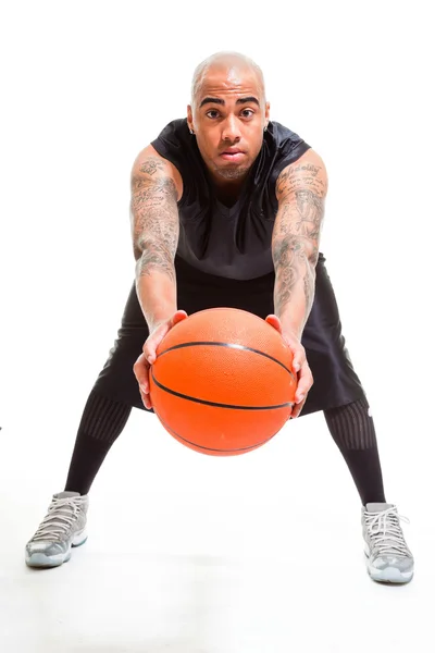 Studioporträt eines Basketballspielers, der isoliert auf weiß steht und Ball hält. Tätowierungen auf seinen Armen. — Stockfoto