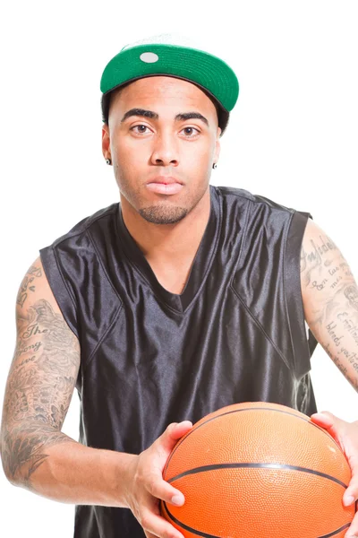 Студійний портрет баскетболіста в зеленій шапці, що стоїть і тримає м'яч ізольовано на білому. Татуювання на руках . — стокове фото