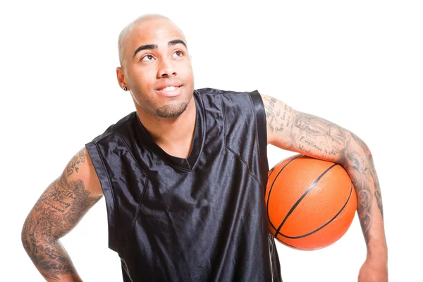 Portret van een jonge basketbalspeler die permanent met een bal tegen witte achtergrond. studio opname. tatoeages op zijn armen. — Stockfoto
