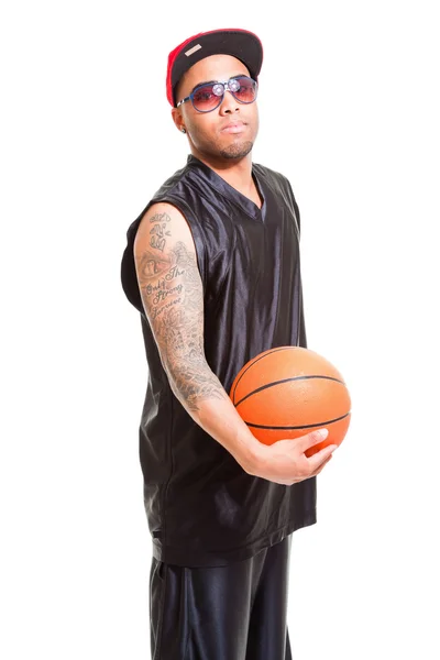 Studio portret van basketbalspeler dragen Pet en zonnebril permanent en houden bal geïsoleerd op wit. tatoeages op zijn armen. — Stockfoto