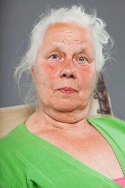Šťastný uvolněný starší žena s šedé dlouhé vlasy sedí v křesle. Studio záběr izolované na šedém pozadí. — Stock fotografie