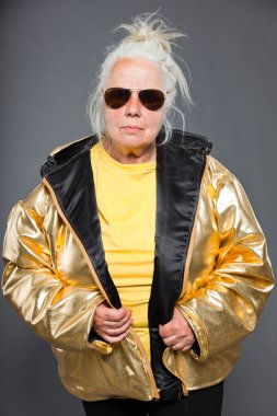 Cool senior mujer chaqueta dorada. pelo largo gris. gafas de sol. estudio de tiro. aislado.