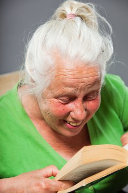 kadın kıdemli oturma koltuğu kitap okuyorum. gri uzun saçlı. izole üzerinde gri arka plan stüdyo vurdu.