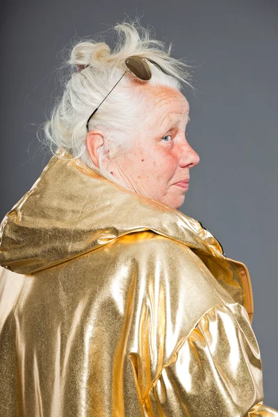 Cool senior vrouw dragen gouden jas. lang grijze haren. zonnebril. studio opname. geïsoleerd. — Stockfoto