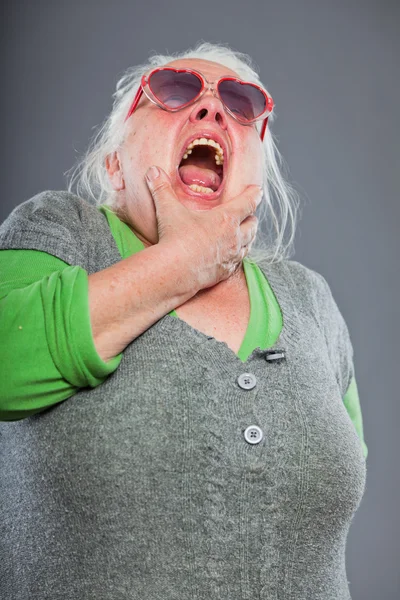 Senior vrouw dragen van een zonnebril met expressief gezicht. grappig. studio opname geïsoleerd op grijze achtergrond. — Stockfoto
