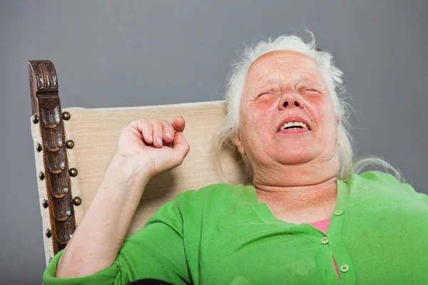 Glad avslappnad senior kvinna med grå långt hår som sitter i stol. Studio skott isolerade på grå bakgrund. — Stockfoto