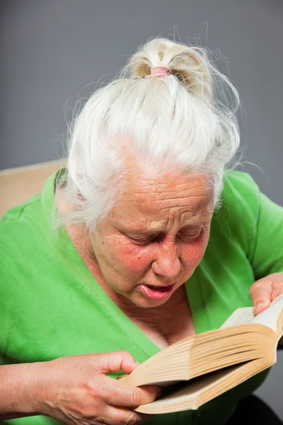 Senior woman sitting chair reading a book. Grey long hair. Studio shot isolated on grey background. — Stock Photo, Image