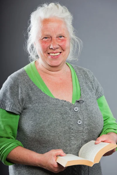 Seniorin mit weißgrauen Haaren liest ein Buch. Studioaufnahme isoliert auf grauem Hintergrund. — Stockfoto