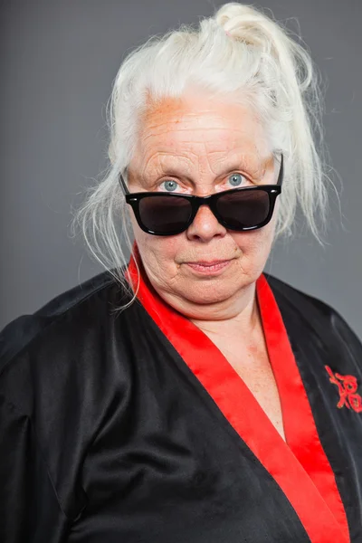 黒と赤の着物および黒いサングラスを身に着けて灰色の長い髪を持つ年配の女性。格好いい。スタジオ撮影に分離の灰色の背景. — ストック写真