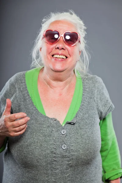 Donna anziana con occhiali da sole dal viso espressivo. Divertente. Studio girato isolato su sfondo grigio . — Foto Stock