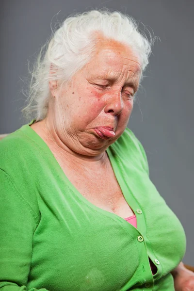 Glücklich entspannte Seniorin mit grauen langen Haaren im Stuhl sitzend. Studioaufnahme isoliert auf grauem Hintergrund. — Stockfoto