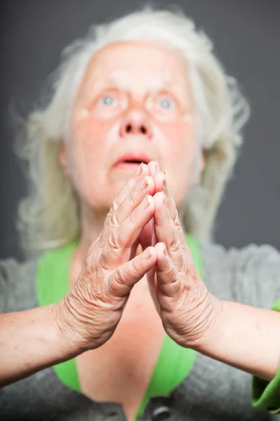 Seniorin mit weißgrauen Haaren in spirituellen Posen. ausdrucksstarkes Gesicht und Hände. Studioaufnahme isoliert auf grauem Hintergrund. — Stockfoto