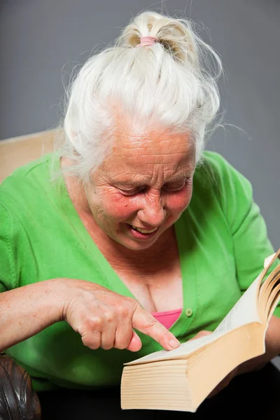 Senior mulher sentada cadeira lendo um livro. Cabelo longo cinzento. Estúdio tiro isolado em fundo cinza . — Fotografia de Stock