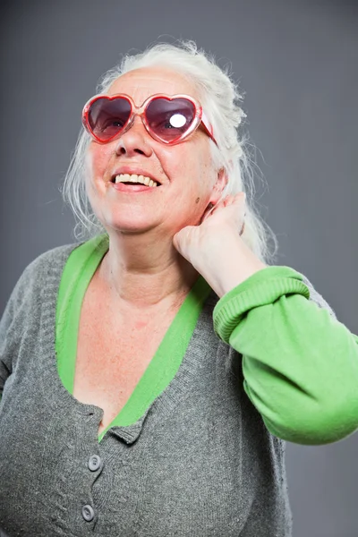 Senior woman with sunglasses deaf. Bad hearing. Hip and cool looking. Studio shot. Isolated on grey background. — Stock Photo, Image