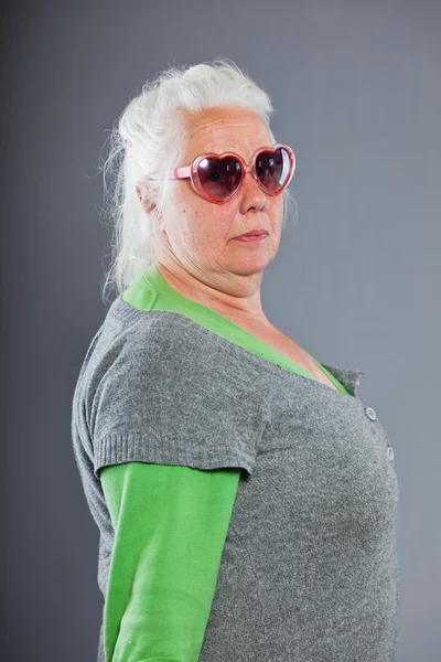Mulher sênior com óculos de sol fazendo caras engraçadas. Expressivo. Estúdio tiro isolado em fundo cinza . — Fotografia de Stock