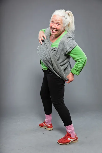 Mulher idosa expressiva engraçada. A agir jovem. Estúdio tiro isolado em fundo cinza . — Fotografia de Stock