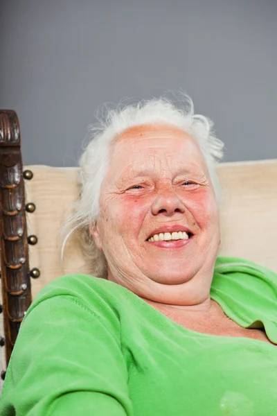 Szczęśliwy, zrelaksowany starszy kobieta z siwe włosy długo siedzi w fotelu. Studio strzał na białym tle na szarym tle. — Zdjęcie stockowe