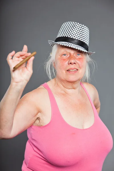 Старша жінка носить капелюх і курить сигару. Прохолодний і хіп-хоп погляд. Студійний знімок ізольовано на сірому фоні . — стокове фото