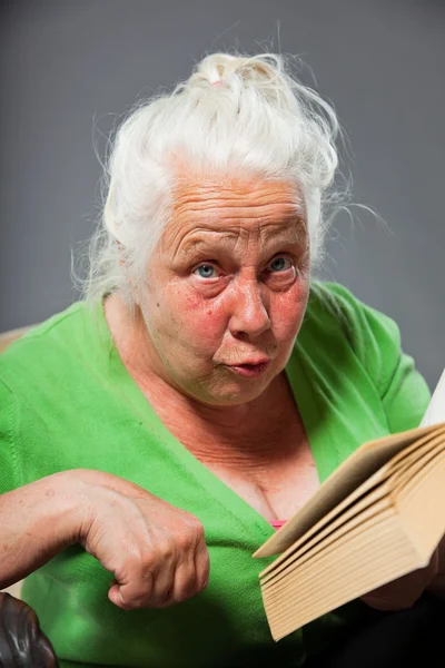 Senior vrouw vergadering stoel het lezen van een boek. grijze lange haren. studio opname geïsoleerd op grijze achtergrond. — Stockfoto
