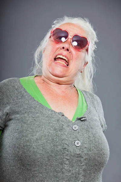 Starší žena nosí sluneční brýle s výraznou tvář. Legrační. Studio záběr izolované na šedém pozadí. — Stock fotografie