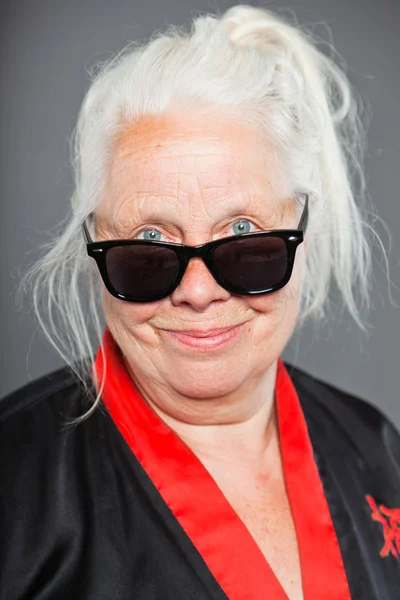 Femme âgée aux longs cheveux gris portant du kimono noir et rouge et des lunettes de soleil noires. Sympa. Studio tourné isolé sur fond gris . — Photo