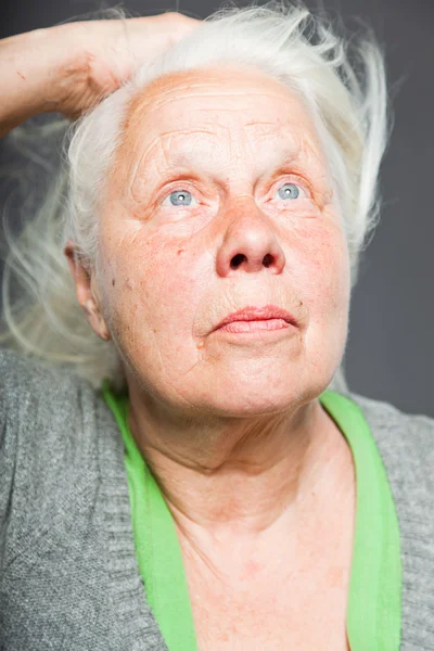 Femme âgée tenant la main dans les cheveux. Un regard spirituel. Studio tourné isolé sur fond gris . — Photo