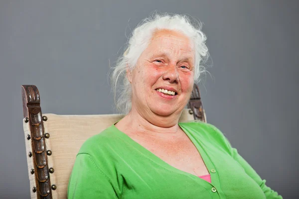 Счастливая расслабленная пожилая женщина с седыми длинными волосами, сидящая в кресле. Съемка изолирована на сером фоне . — стоковое фото