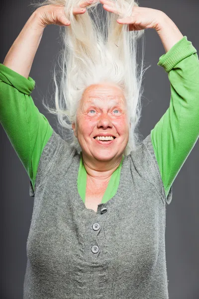 Seniorin hält Hände in den Haaren. spirituell aussehend. Studioaufnahme isoliert auf grauem Hintergrund. — Stockfoto