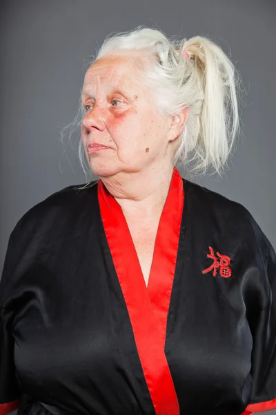 Senior vrouw met lang grijze haren dragen zwarte en rode kimono. studio opname geïsoleerd op grijze achtergrond. — Stockfoto