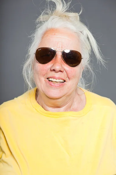 Cool hip starší žena s sluneční brýle a dlouhé šedivé vlasy. výraznou tvář. Studio záběr izolované na grey. — Stock fotografie