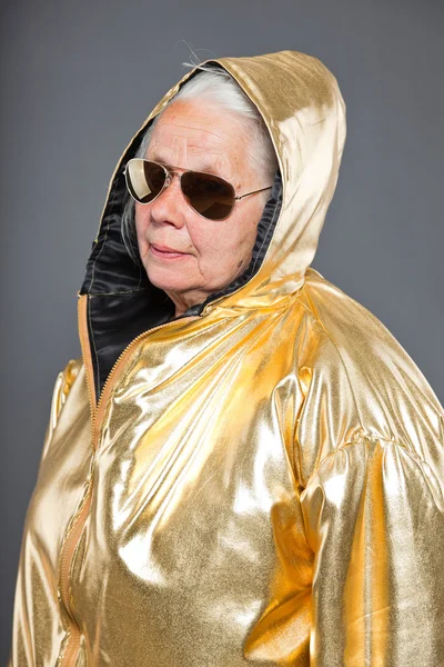 Mulher sênior legal vestindo casaco dourado. Cabelo longo e cinzento. Óculos de sol. Tiro no estúdio. Isolados . — Fotografia de Stock