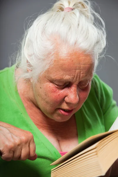 Senior mulher sentada cadeira lendo um livro. Cabelo longo cinzento. Estúdio tiro isolado em fundo cinza . — Fotografia de Stock