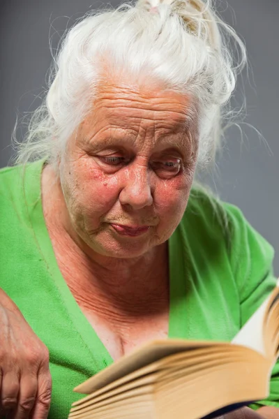Femme âgée assise chaise lisant un livre. Cheveux longs gris. Studio tourné isolé sur fond gris . — Photo