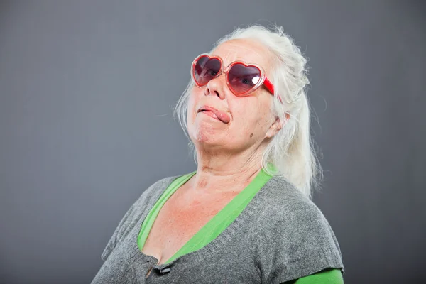 Seniorin mit Sonnenbrille macht lustige Gesichter. Ausdrucksstark. Studioaufnahme isoliert auf grauem Hintergrund. — Stockfoto
