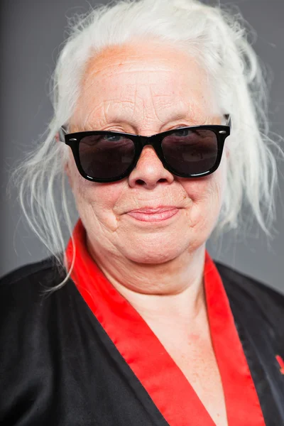 Mujer mayor con el pelo largo y gris usando kimono negro y rojo y gafas de sol negras. Bonito aspecto. Estudio plano aislado sobre fondo gris . — Foto de Stock