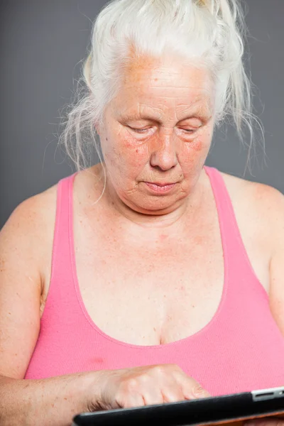 Äldre kvinna med tabletten långt grått hår. Studio skott. isolerad på grå bakgrund. — Stockfoto