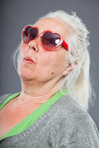 Idősebb nő, napszemüveg, hogy vicces arcok. kifejező. stúdió felvétel elszigetelt a szürke háttér. — Stock Fotó