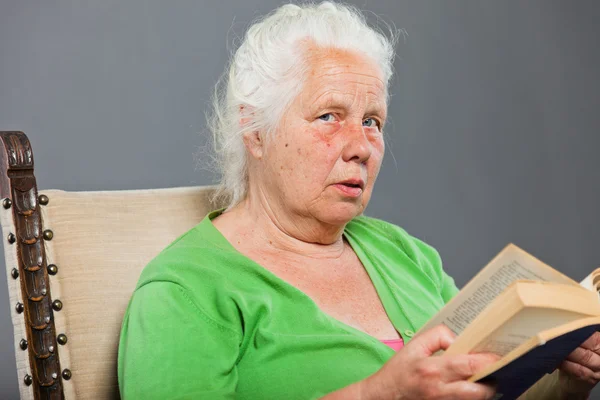 Seniorin sitzt Stuhl und liest ein Buch. graue lange Haare. Studioaufnahme isoliert auf grauem Hintergrund. — Stockfoto