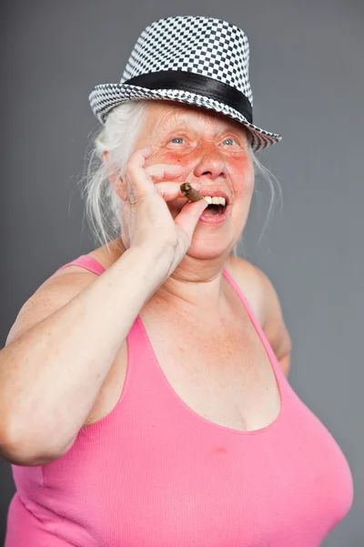 Äldre kvinna som bär hatt och röka cigarr. cool och höft letar. Studio skott isolerade på grå bakgrund. — Stockfoto